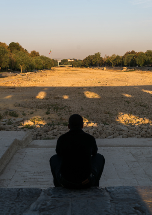Iranian man sit on Khaju bridge Pol-e Khaju looking the  dry Zayandeh river, Isfahan Province, Isfahan, Iran