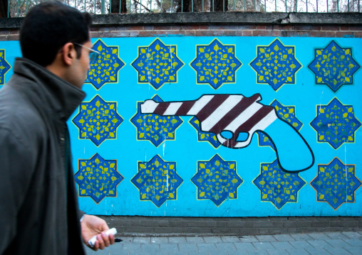 man passing in front of anti-american mural propoganda on the wall of the former united states embassy, Central district, Tehran, Iran