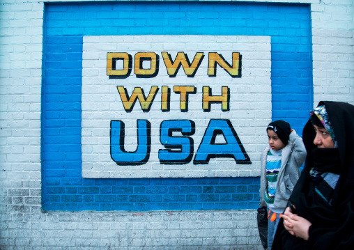 people passing in front of anti-american mural propoganda on the wall of the former united states embassy, Central district, Tehran, Iran