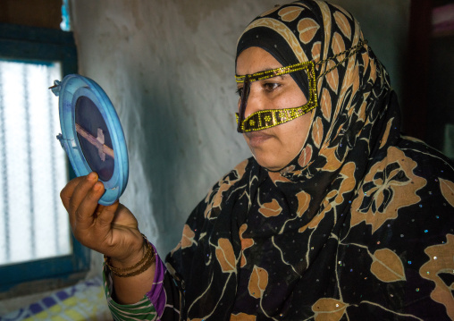 a bandari woman wearing a traditional mask looking herself in a mirror, Qeshm Island, Salakh, Iran