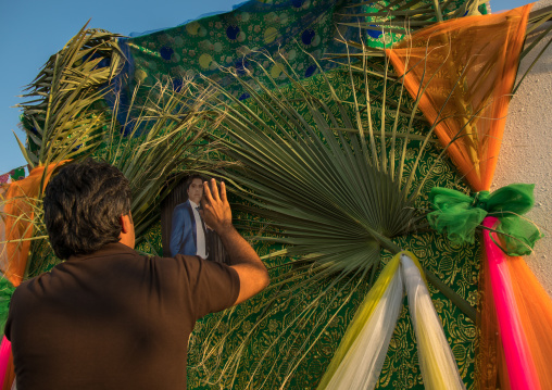man putting the picture of the groom on a wall during a wedding, Hormozgan, Kushkenar, Iran