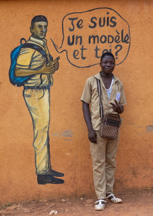 African boy standing in front of a mural depicting a pupil who works well at school, Savanes district, Boundiali, Ivory Coast