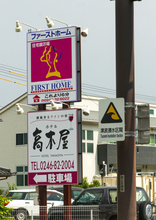 A sign on a coastal road warns people about tsunami bewtweens hotel and real estate ads, Fukushima prefecture, Tairatoyoma beach, Japan