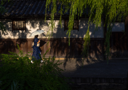 Japanese woman with an umbrella passing in front old houses along the riverbank, Okayama Prefecture, Kurashiki, Japan