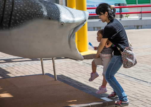 Mother holding her child to let her inside a fake giant plastic whale shark in Kaiyukan aquarium, Kansai region, Osaka, Japan