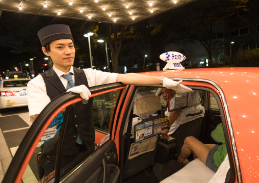 Japanese hotel employee opens taxi door and put his hand to avoid head shock, Kanto region, Tokyo, Japan
