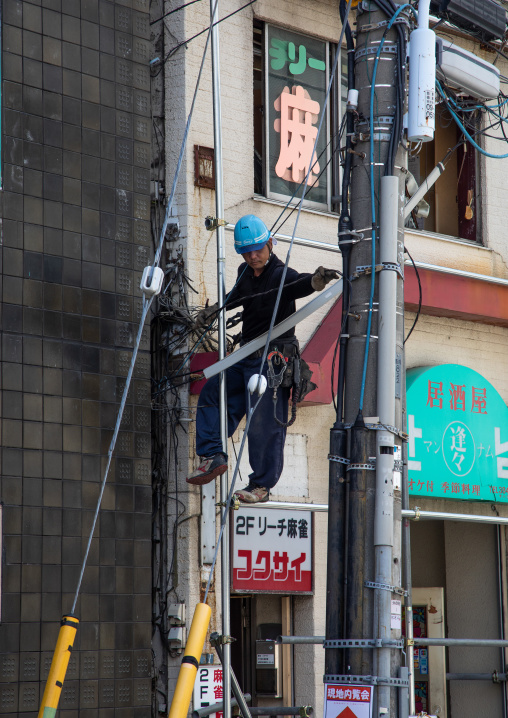 Low angle view of technician repairing electric pole, Kanto region, Tokyo, Japan