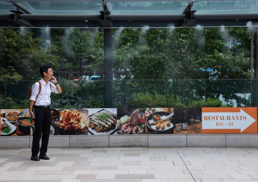 Japanese man on the phone searching for freshness under a water spray, Kanto region, Tokyo, Japan