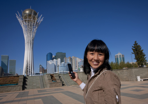 Ethnic Kazakh Girl With Cellphone In Front Of Baiterek Tower, Astana, Kazakhstan"