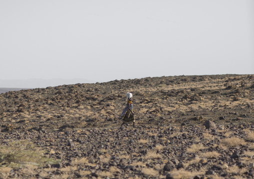 Turkana woman carrying a bag on her head and crossing an arid area, Turkana lake, Loiyangalani, Kenya