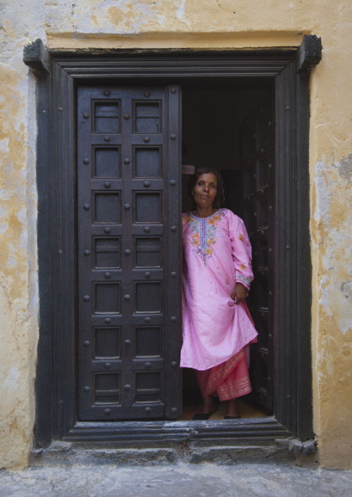 Woman standing in the frame of a wooden carved door, Lamu County, Lamu, Kenya