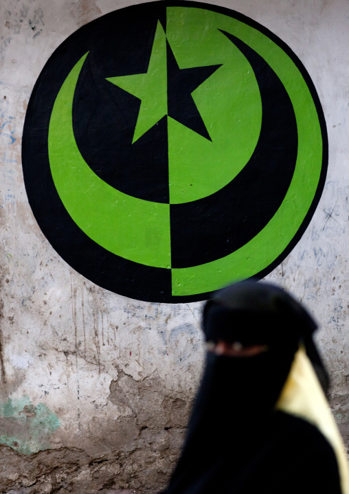 Muslim woman in niqab passing by a muslim crescent and star sign in the street, Lamu County, Lamu, Kenya