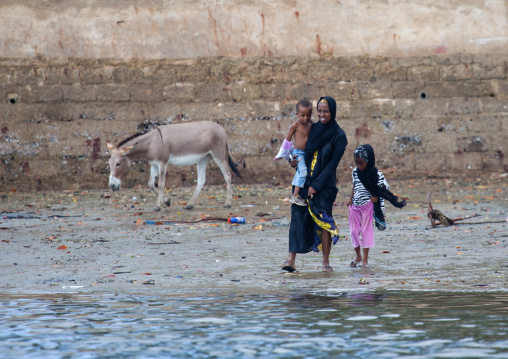 Muslim woman walking on a dirty beach with her children, Lamu County, Lamu, Kenya