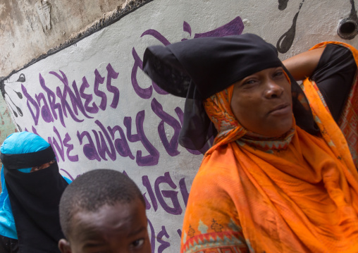 Mulsim people passing in front of a wall covered with graffitis, Lamu county, Lamu town, Kenya
