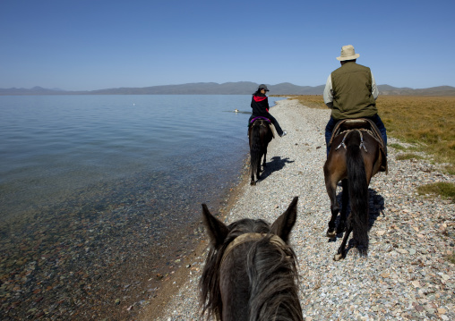 Woman And Western Man Riding Horses Along The Bank Of Song Kol Lake, Jaman Echki Jailoo, Kyrgyzstan