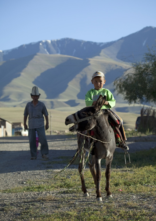 Old Man With Kalpak Hat Looking At A Young Boy Riding A Donkey, Kochkor, Kyrgyzstan
