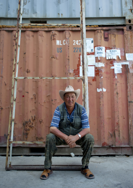 Man With A Cow Boy Hat Sitting In Front Of A Container In Dordoi Market, Bishkek, Kyrgyzstan