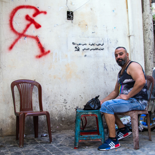 Lebanese man sit in the street in front of a communist party tag on a wall in el Mina, North Governorate, Tripoli, Lebanon