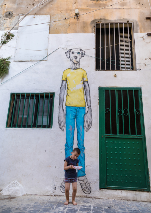 Lebanese kid standing in front of a giant dog painting in the street, South Governorate, Tyre, Lebanon