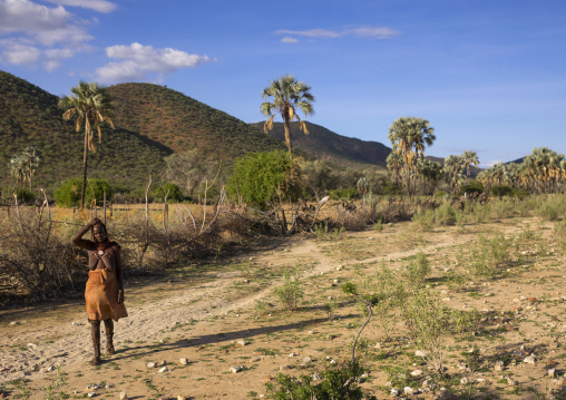 Himba Woman In Front Of Palms Trees In An Arid Landscape, Epupa, Namibia