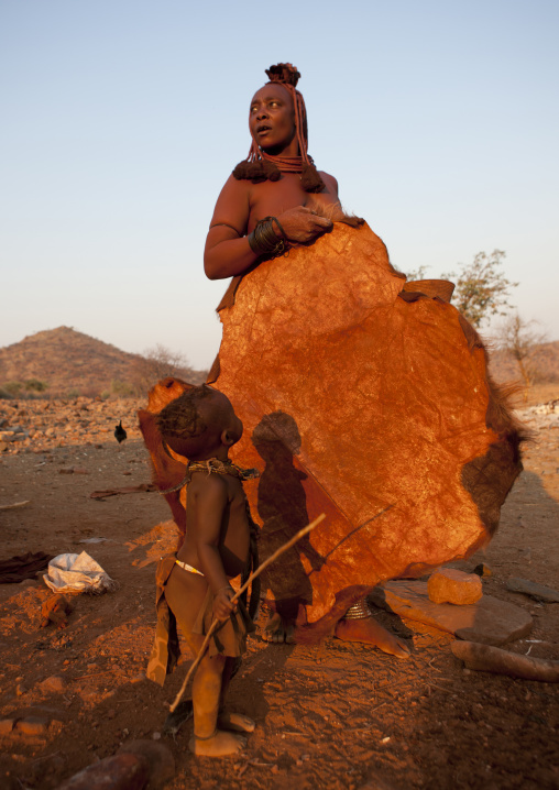 Himba Kid Looking At His Mother Holding A Skin, Okapale Area, Namibia