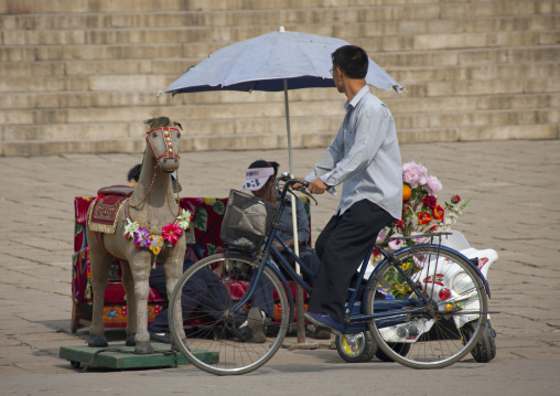 North Korean man on a bicycle in front of a street photo studio with a fake horse, Pyongan Province, Pyongyang, North Korea
