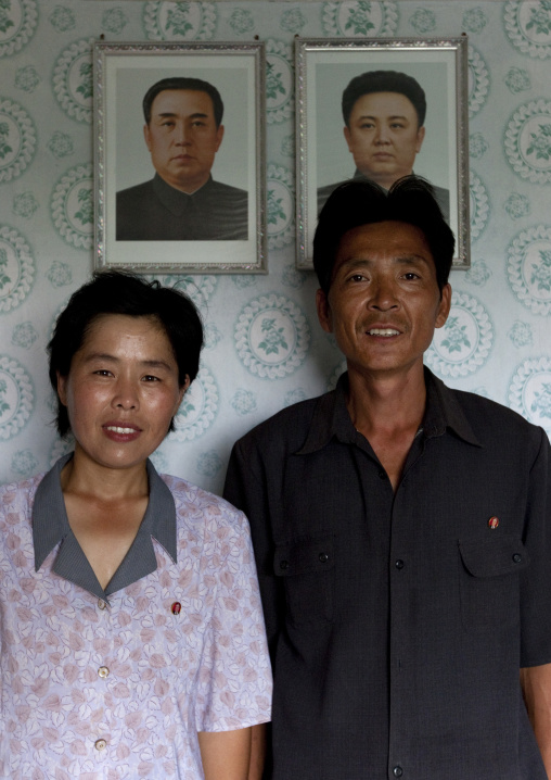 Smiling North Korean couple in front of the official portraits of the Dear Leaders in their house, Kangwon Province, Chonsam Cooperative Farm, North Korea