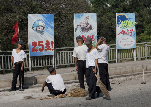 North Korean young men cleaning the road in front of propaganda posters, Pyongan Province, Pyongyang, North Korea