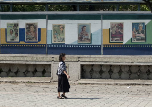 North Korean woman passing in front movie posters in the street, Pyongan Province, Pyongyang, North Korea