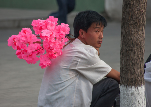 North Korean man going to the celebration of the 60th anniversary of the regim with plastic bunches of red flowers, Pyongan Province, Pyongyang, North Korea