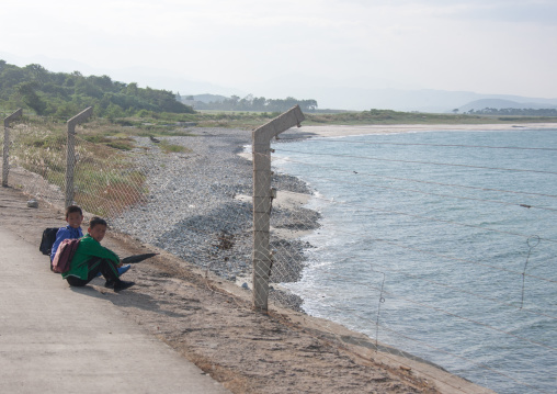 North Korean boys sit in front of a fence on the seaside, North Hamgyong Province, Chilbo Sea, North Korea