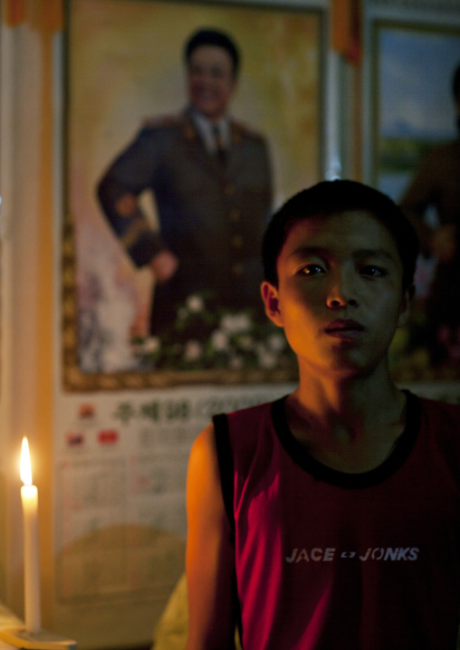 Portrait of a North Korean boy in a candlelit house in front of a Kim Jong-il portrait, North Hamgyong Province, Jung Pyong Ri, North Korea