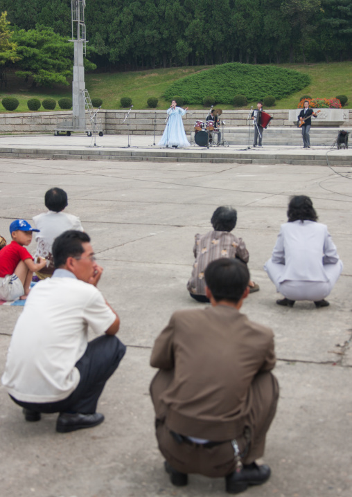 North Korean squatting to listen state artist performing on national day, Pyongan Province, Pyongyang, North Korea