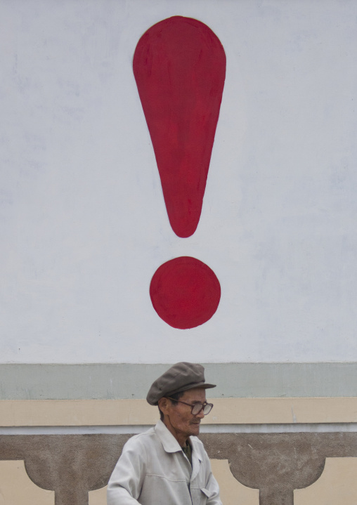 Senior North Korean man walking in the street under an exclamation mark on a wall, North Hwanghae Province, Kaesong, North Korea