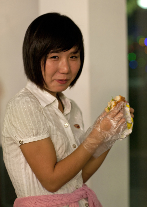 Young North Korean woman eating burger with plastic gloves at Kaeson youth park, Pyongan Province, Pyongyang, North Korea