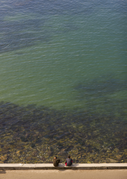 Two North Korean men sitting in front of clear water, Kangwon Province, Wonsan, North Korea