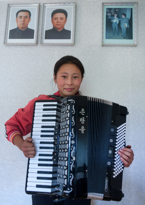 North Korean girl playing accordion under the Dear Leaders portaits, South Pyongan Province, Chonsam Cooperative Farm, North Korea