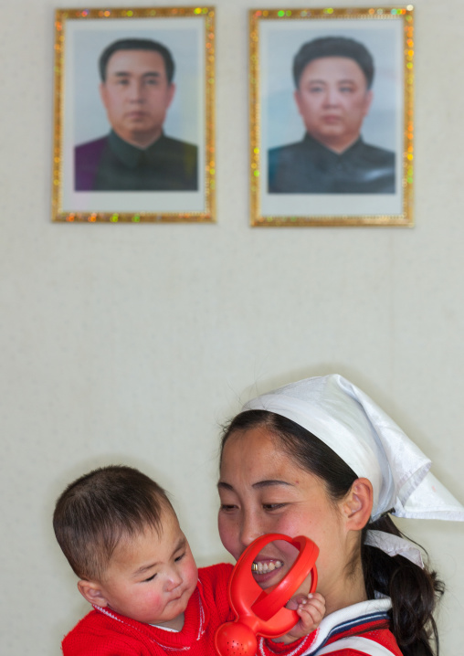 North Korean orphan with a nurse below the portraits of the Dear Leaders, South Pyongan Province, Nampo, North Korea