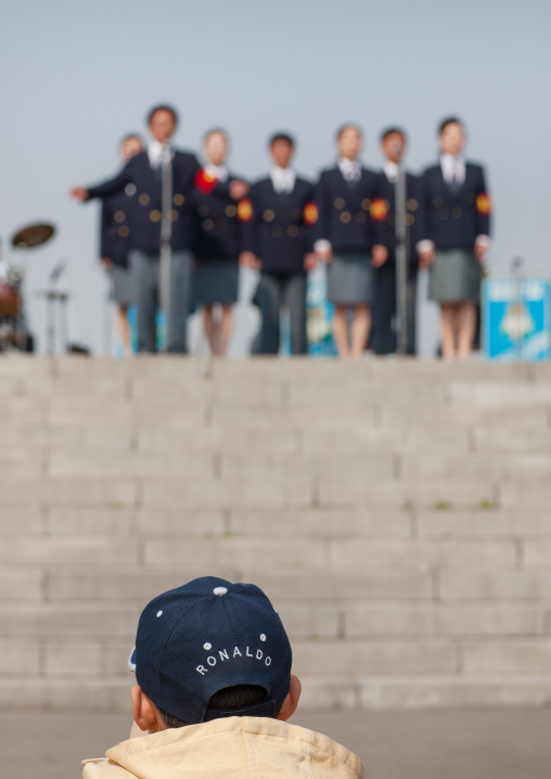 North Korean child with a ronaldo cap looking at a band playing in the international Kimilsungia and Kimjongilia festival, Pyongan Province, Pyongyang, North Korea