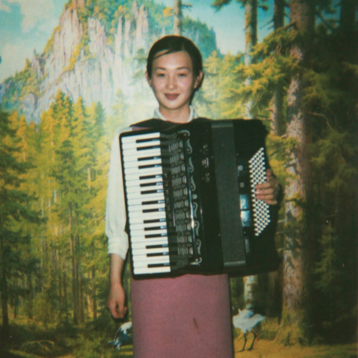 Polaroid of a smiling North Korean waitress playing accordion, Pyongan Province, Pyongyang, North Korea