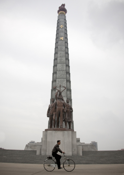 North Korean man cycling in front of the Juche tower built to commemorate Kim il-sung's 70th birthday, Pyongan Province, Pyongyang, North Korea