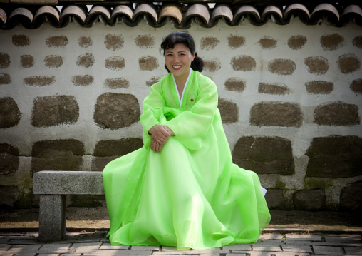 Smiling North Korean woman dressed in green choson-ot sit on a bench, North Hwanghae Province, Kaesong, North Korea