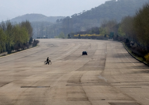 North Korean man with a bicyle crossing an empty highway in North Korea, Pyongan Province, Pyongyang, North Korea
