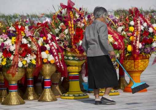 Old North Korean woman cleaning the baskets of flowers in front of the statues of the Dear Leaders in the Grand monument on Mansu hill, Pyongan Province, Pyongyang, North Korea