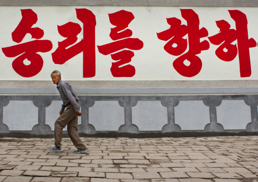 North Korean man passing in front of a propaganda billboard, North Hwanghae Province, Kaesong, North Korea
