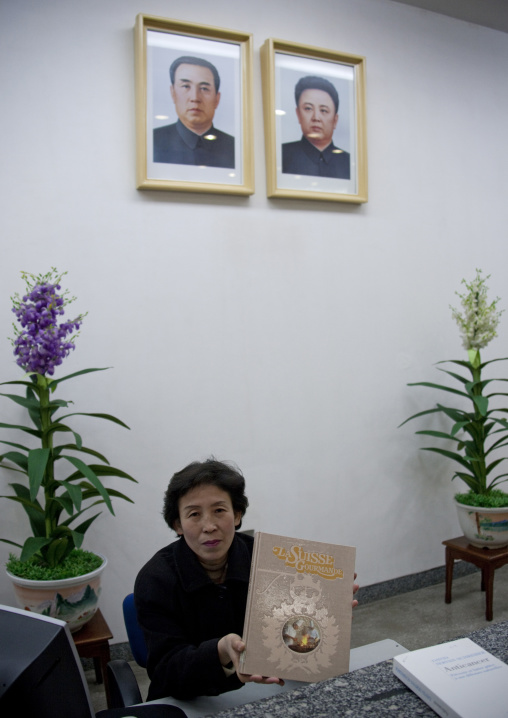 North Korean employee showing a food book in Grand people's study house below the official portraits of the Dear Leaders, Pyongan Province, Pyongyang, North Korea