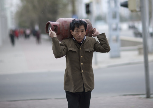 Old North Korean man carrying a gas bottle on his shoulders in the street, Pyongan Province, Pyongyang, North Korea