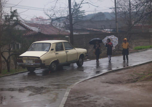 North Korean girls with umbrellas walking near a car under the rain, Pyongan Province, Pyongyang, North Korea