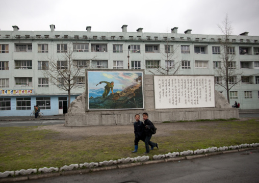 North Korean boys passing by a propaganda billboard depicting a soldier at war, North Hwanghae Province, Kaesong, North Korea