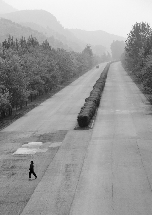 North Korean woman crossing empty highway with a bus arriving in distance, Pyongan Province, Pyongyang, North Korea